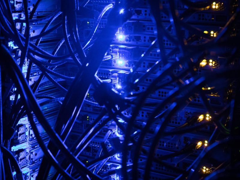 Closeup view of the back of a computer server with blue lights and wires.