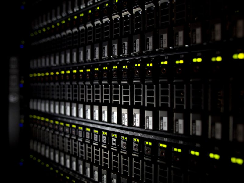 Rows of electronic computer equipment, including lights and displays, in a dark environment.