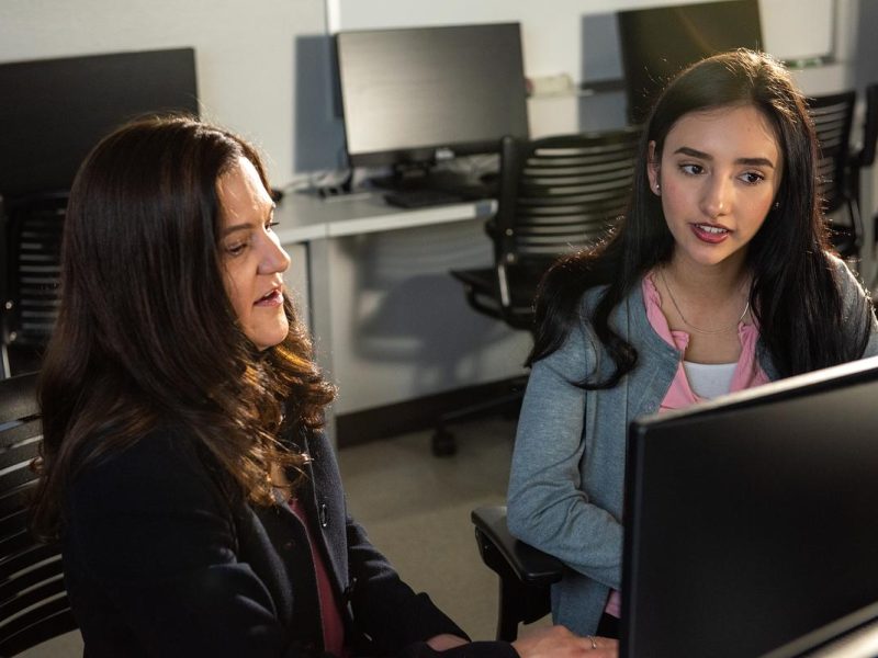 Professor and student engaged in conversation, one gesturing while the other listens.