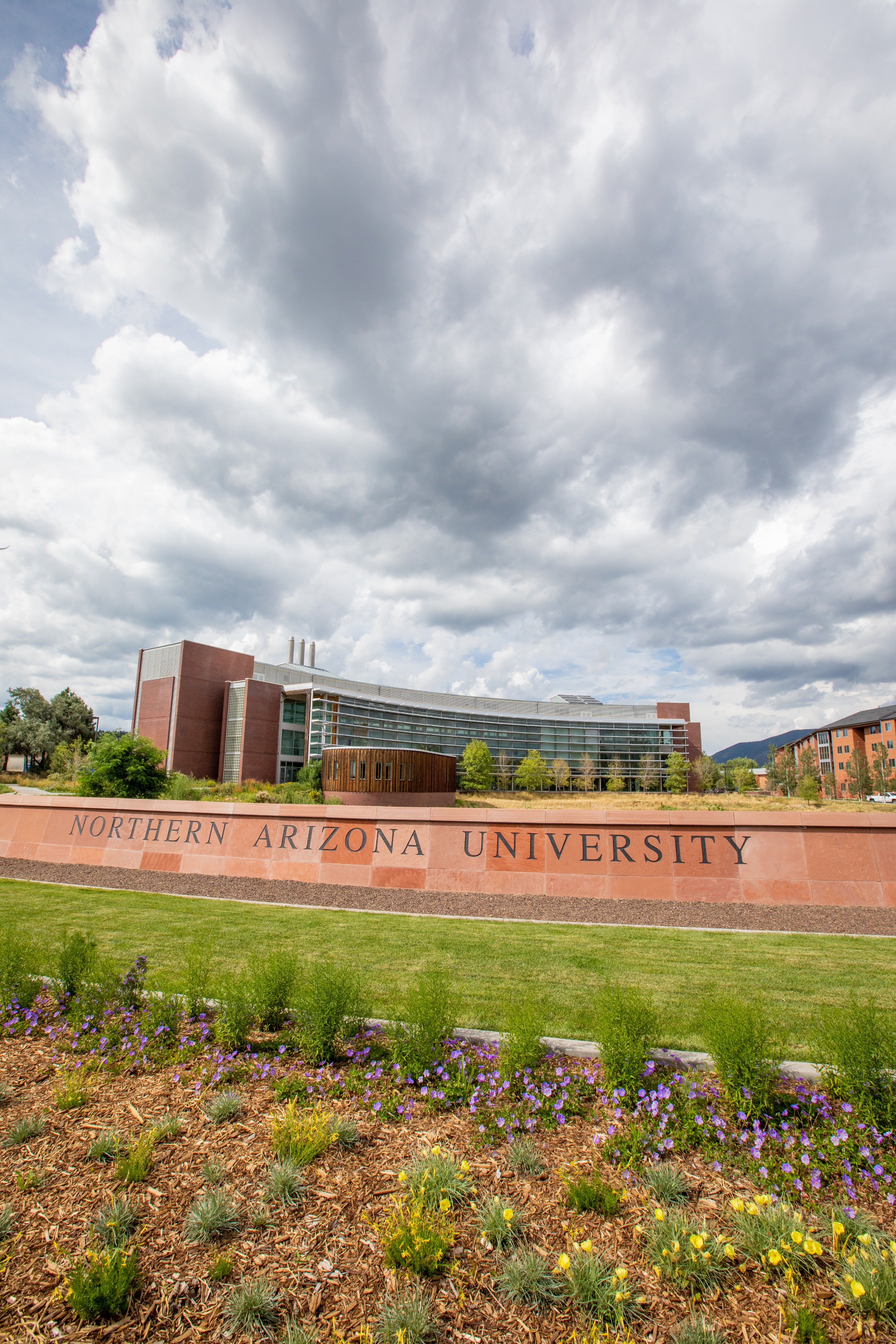 Large brick and glass building with "Northern Arizona University" sign, surrounded by landscaping with flowers and grass, under a cloudy sky.