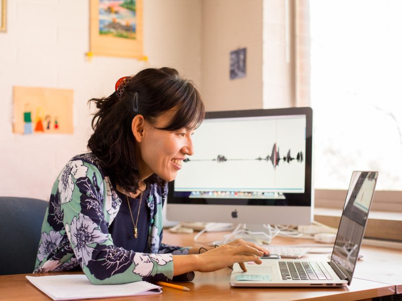 Woman sitting at a desk using a laptop computer, smiling and working in a home office setting.