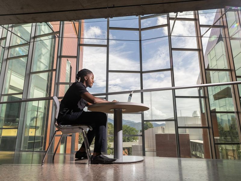 Person sitting at a table in a large glass-enclosed space, with a view of the sky and buildings outside the windows.