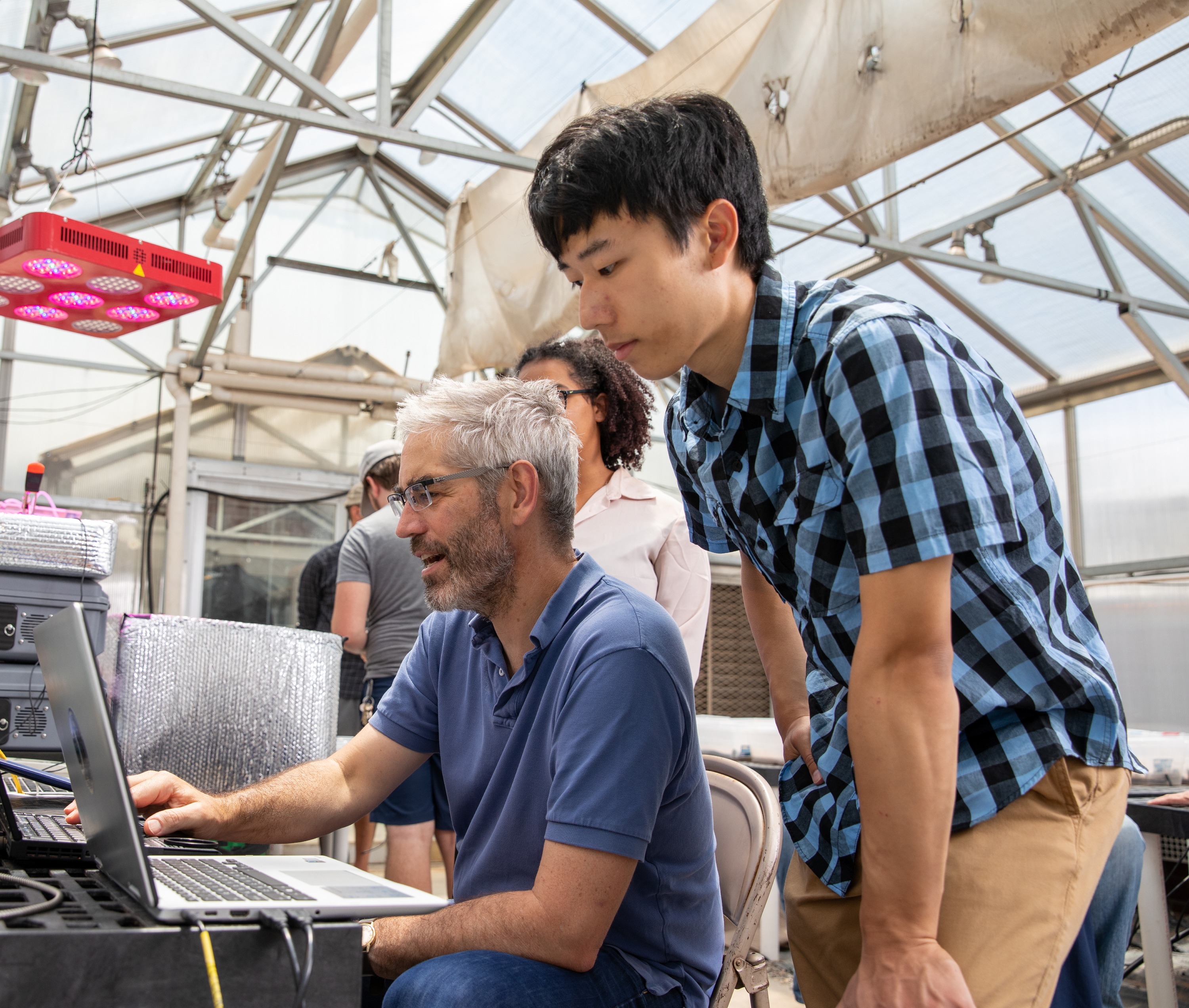 A N A U researcher and student working on computers in a workspace with a technical setup.