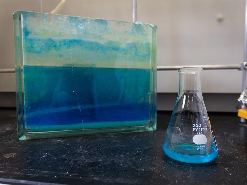 Glass container with blue and green liquid, glass beaker with blue liquid on a black surface.