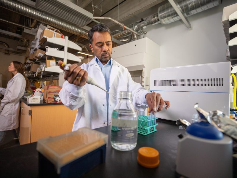 A person in a white laboratory coat working with laboratory equipment and glassware on a counter in a laboratory setting. The person appears to be conducting an experiment or research work.