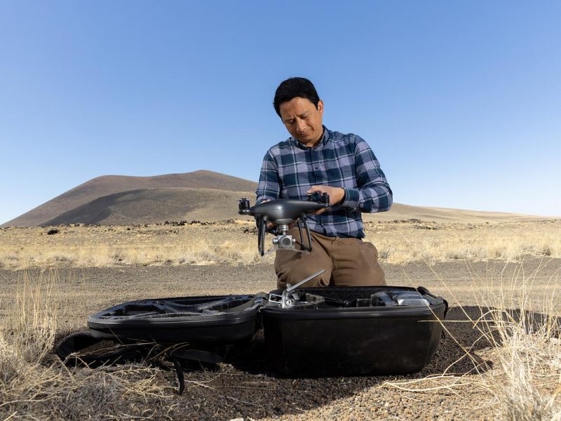Person operating a drone in a desert landscape with hills in the background.