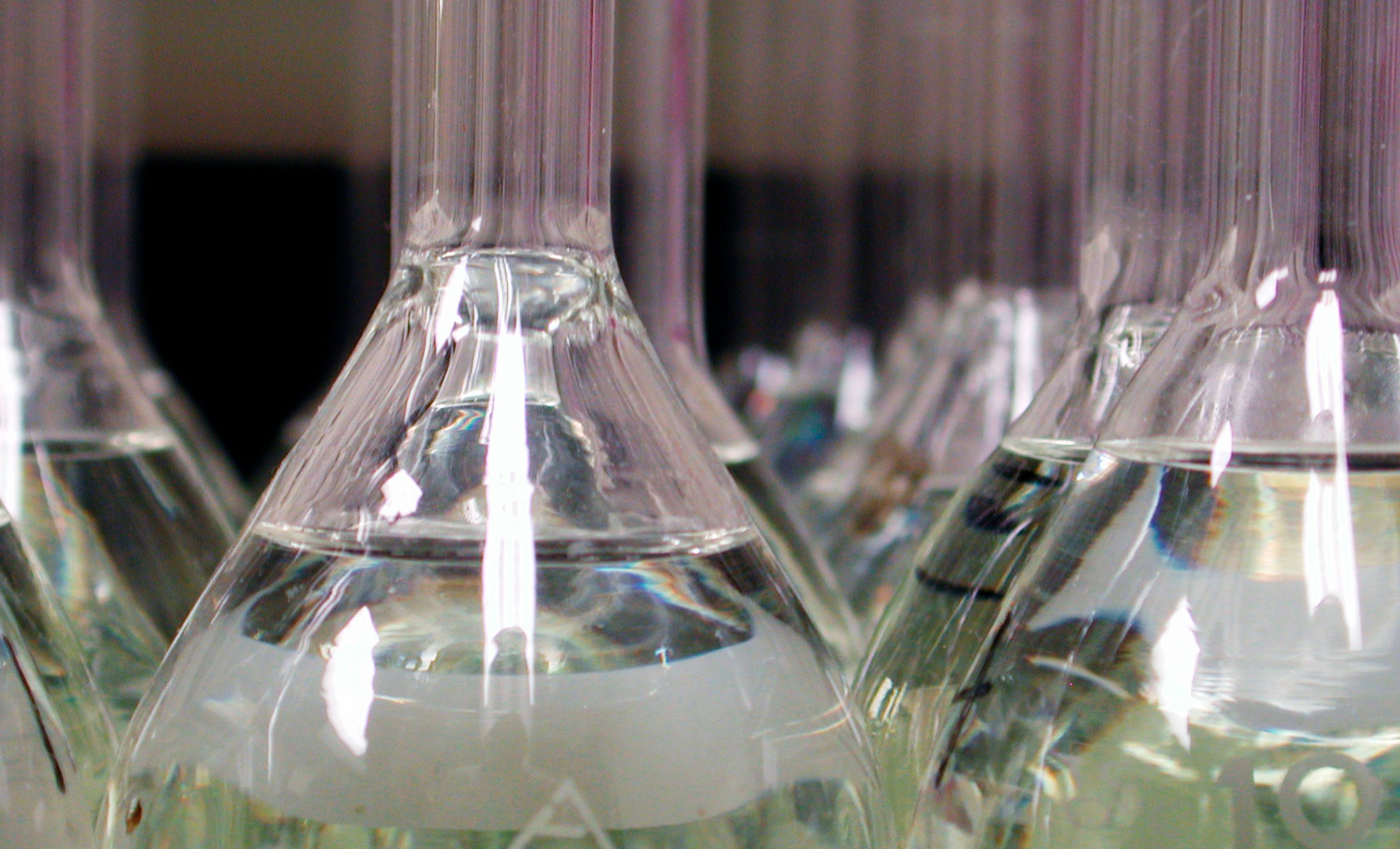 Glass laboratory beakers and flasks filled with a clear liquid, sitting on a dark surface.