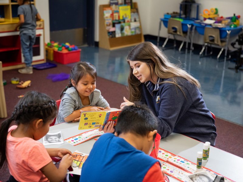 Student teacher helping a student read a book.
