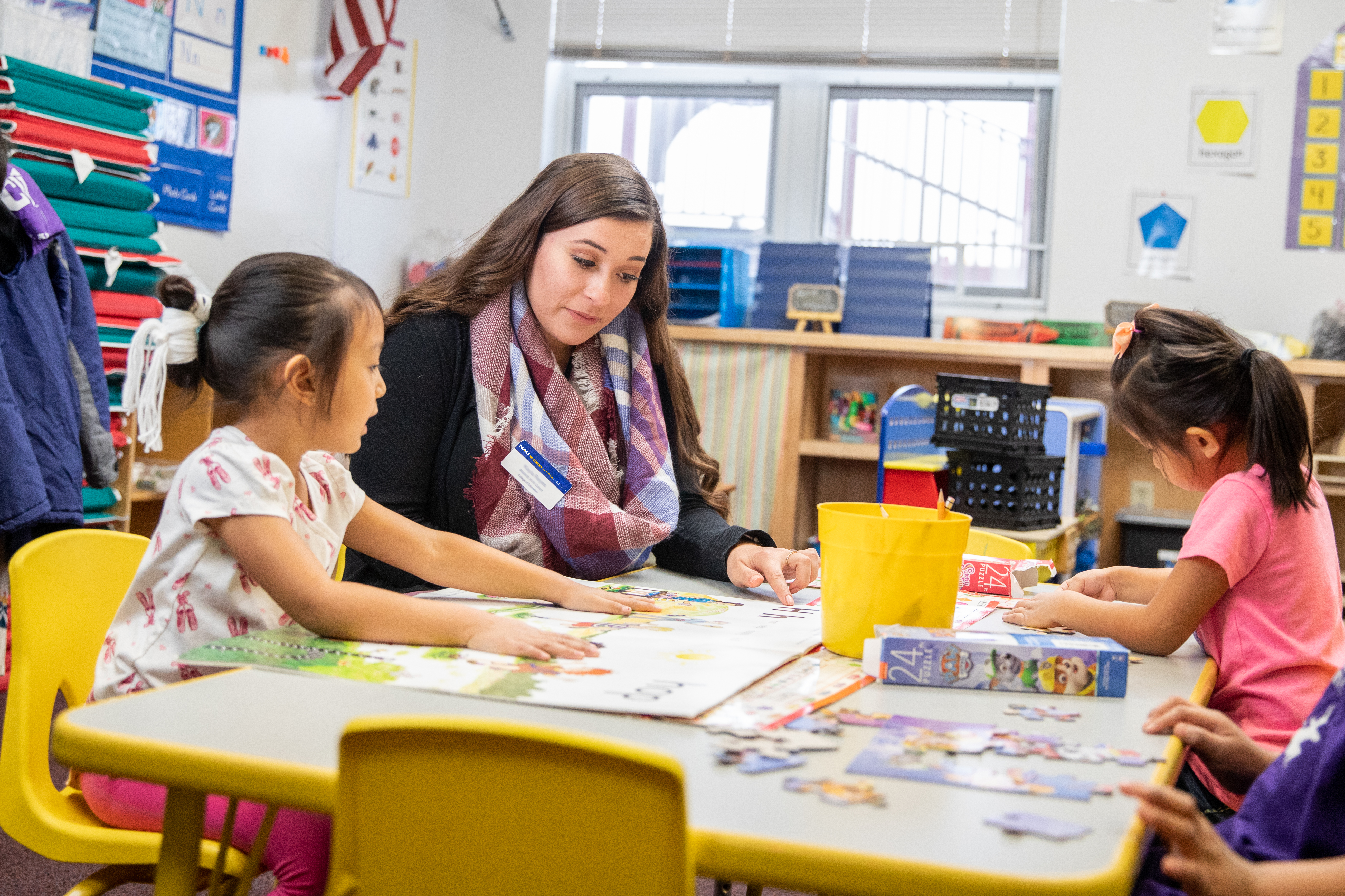 N A U student teacher sitting at table with young students and works on projects.