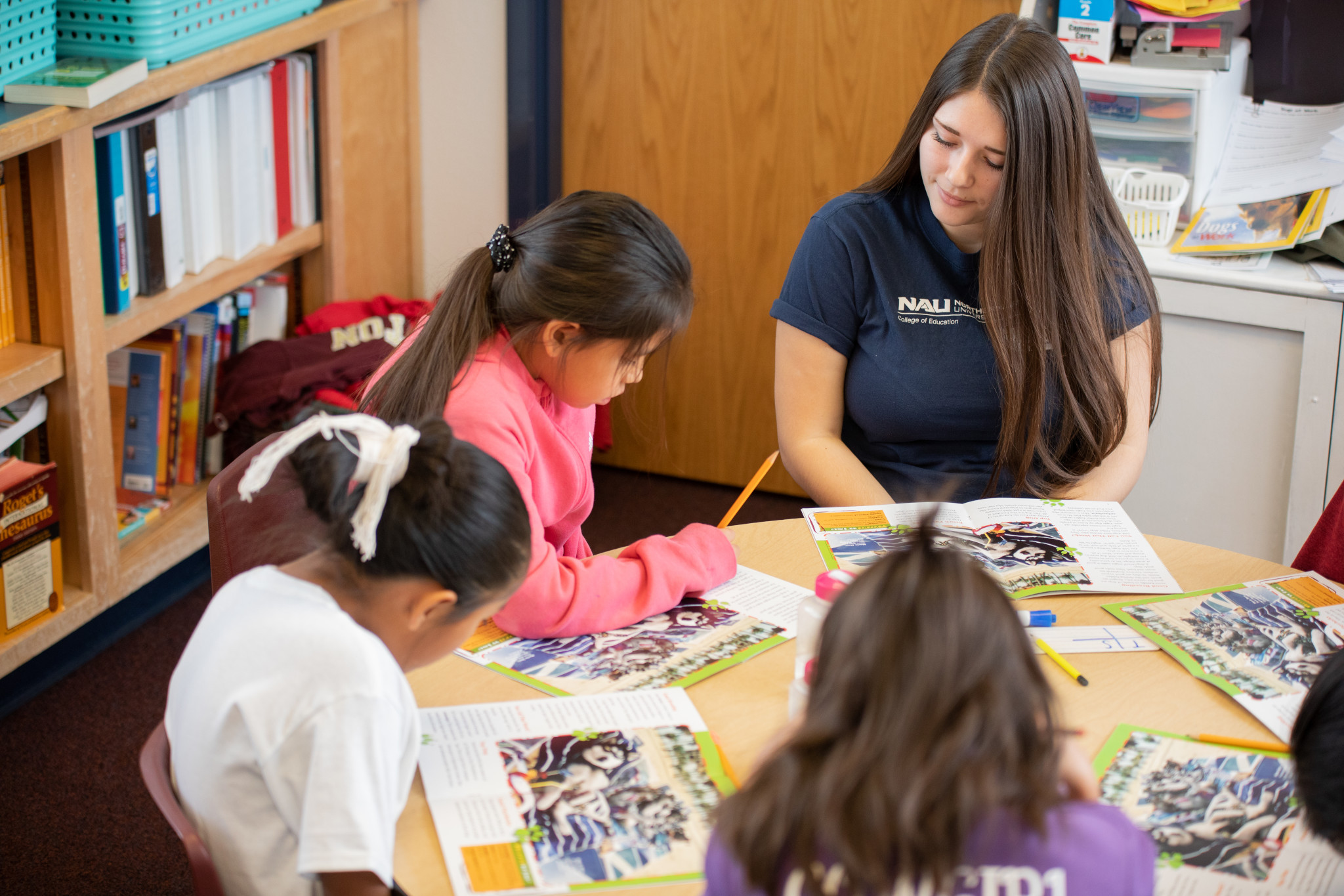 Student teacher sitting with children at a table, reading a book.