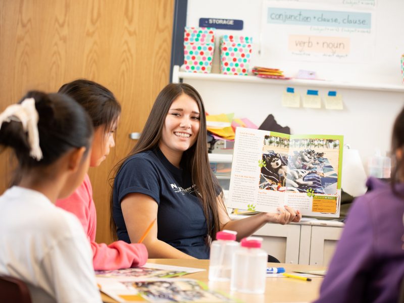 N A U student teacher sits in front of students and reads them a book.