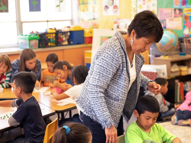 Teacher going around classroom and helping students out.