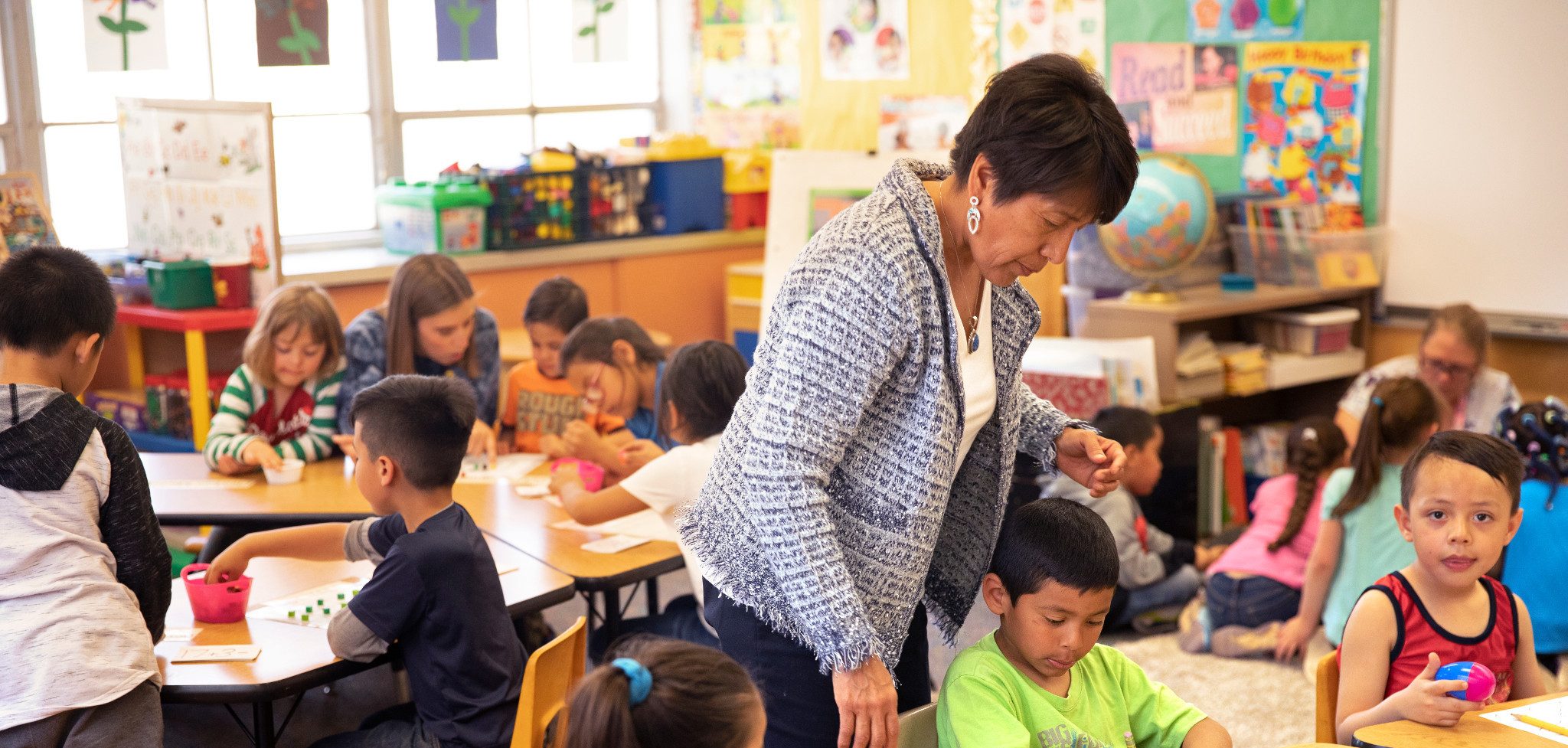 Teacher going around classroom and helping students out.
