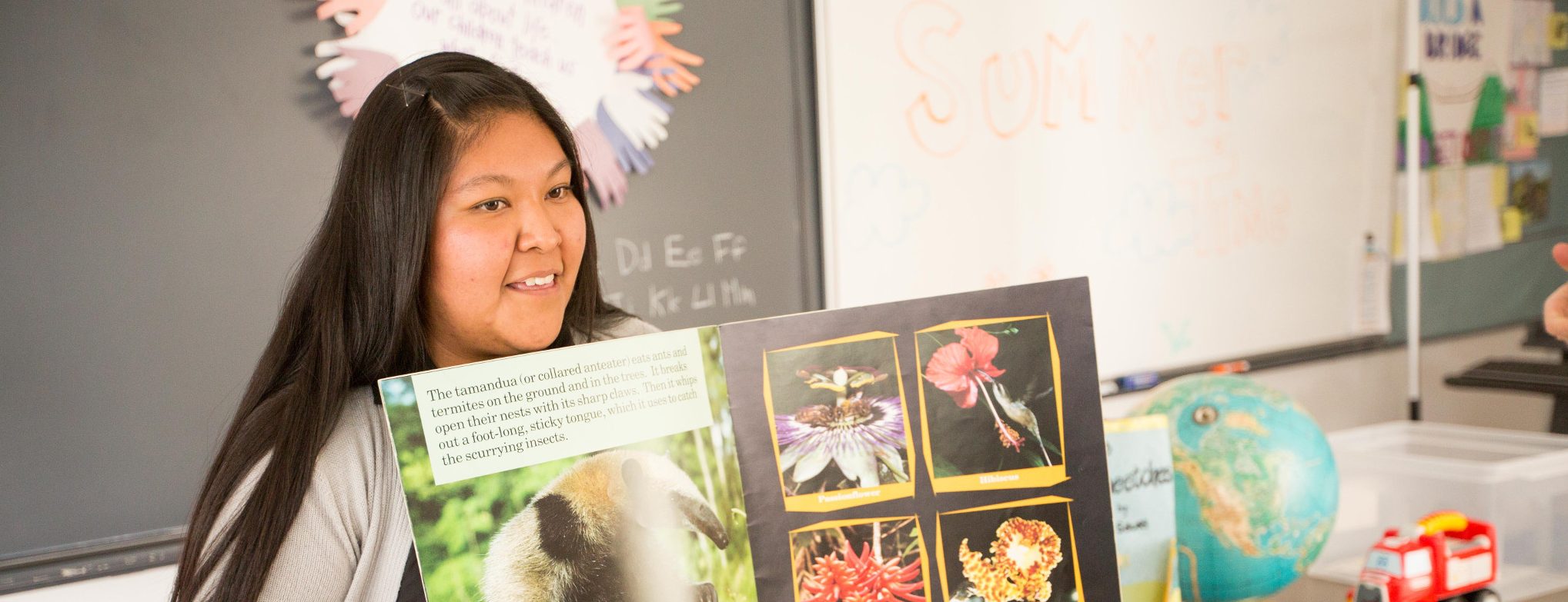 Student teacher sits in front of classroom and reads a book.