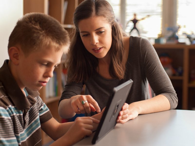 Student teacher teaches child how to use tablet.