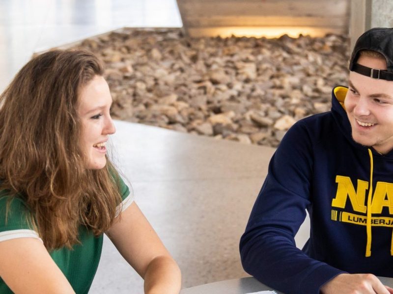 Two N A U students sitting at a table talking to each other.