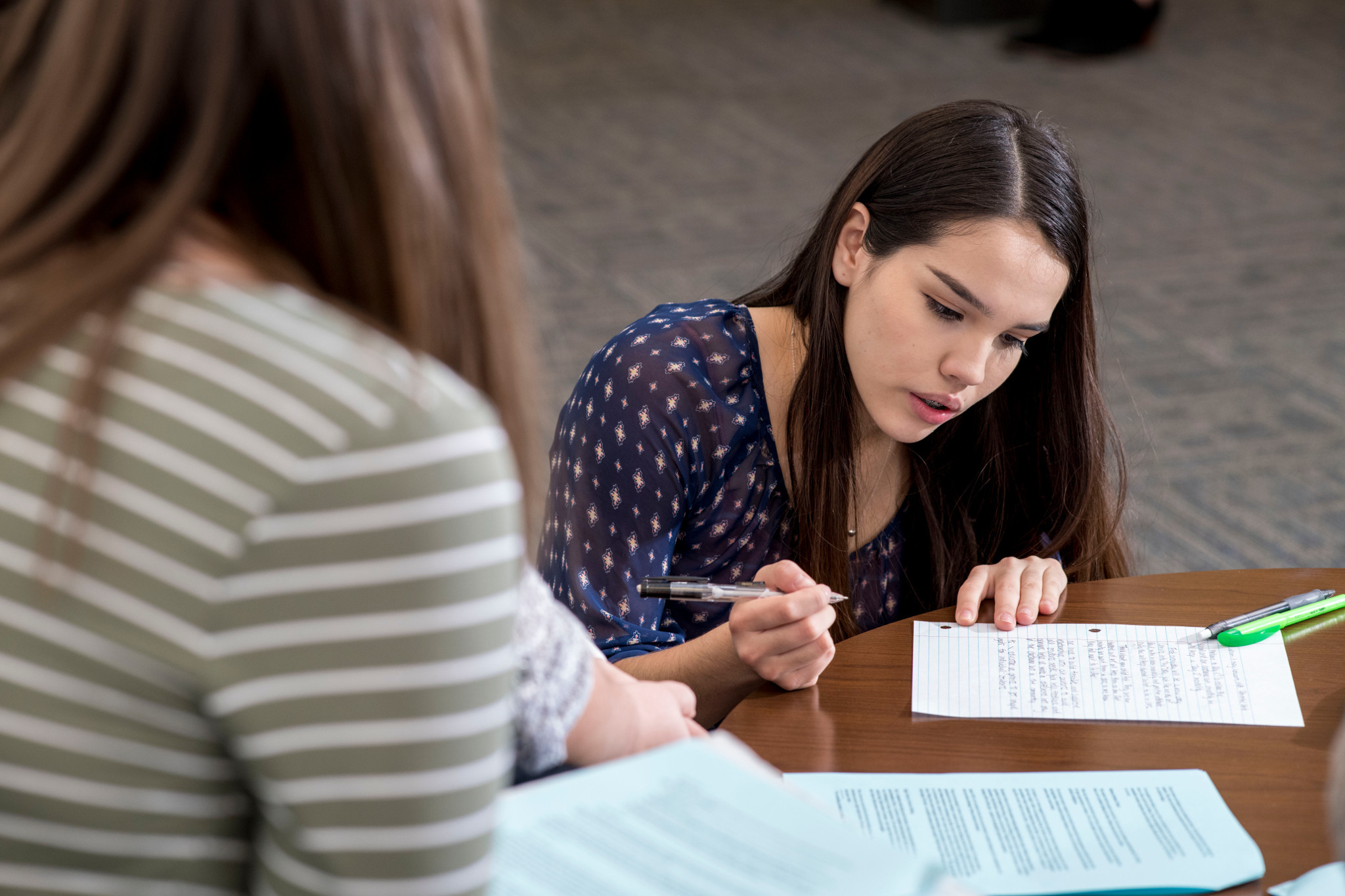 Two students sitting at a table, one of the students is writing on a paper.