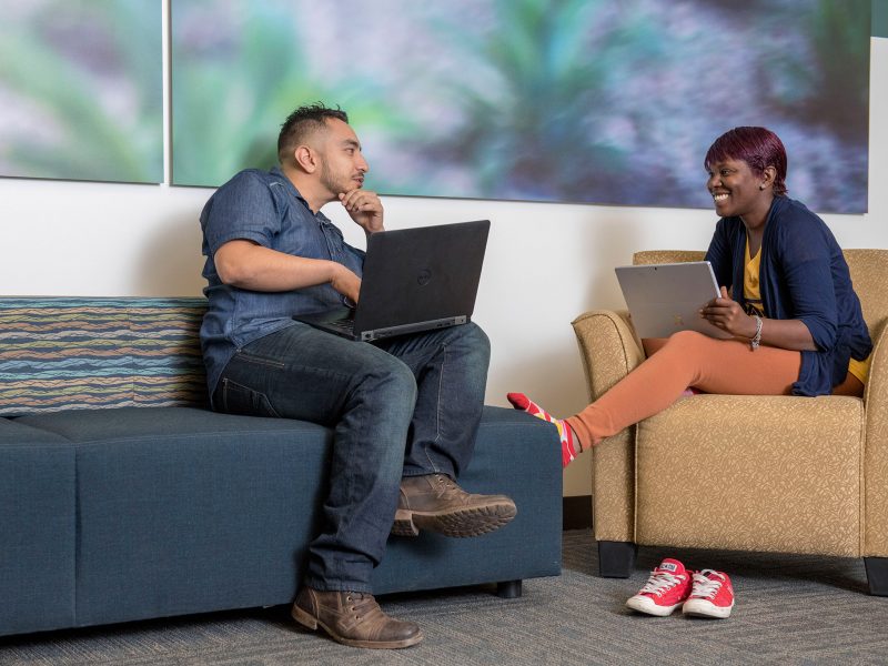 N A U students talking and working together on their laptops in a lounge.
