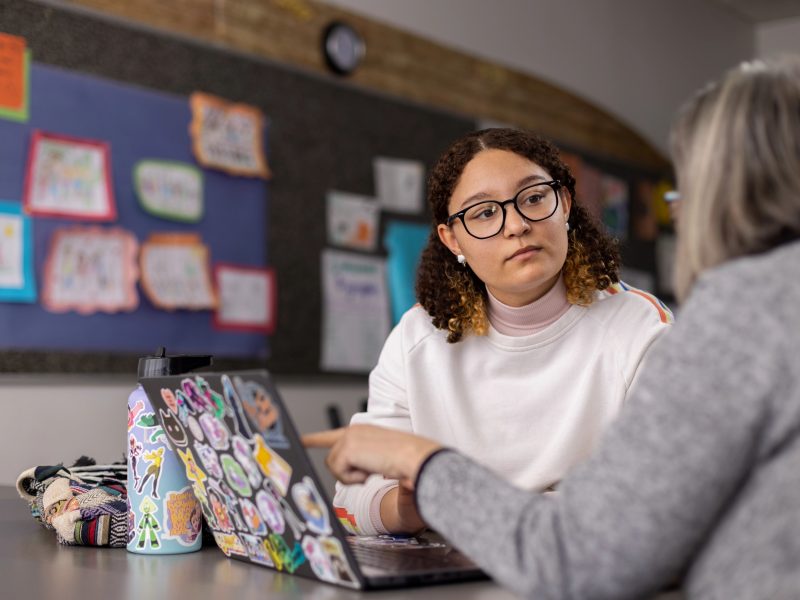 N A U professor and student sitting at a table talking to each other.