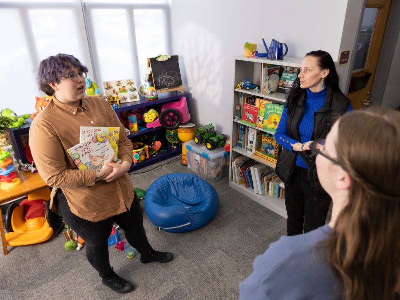 Three people standing in a classroom talking to each other.