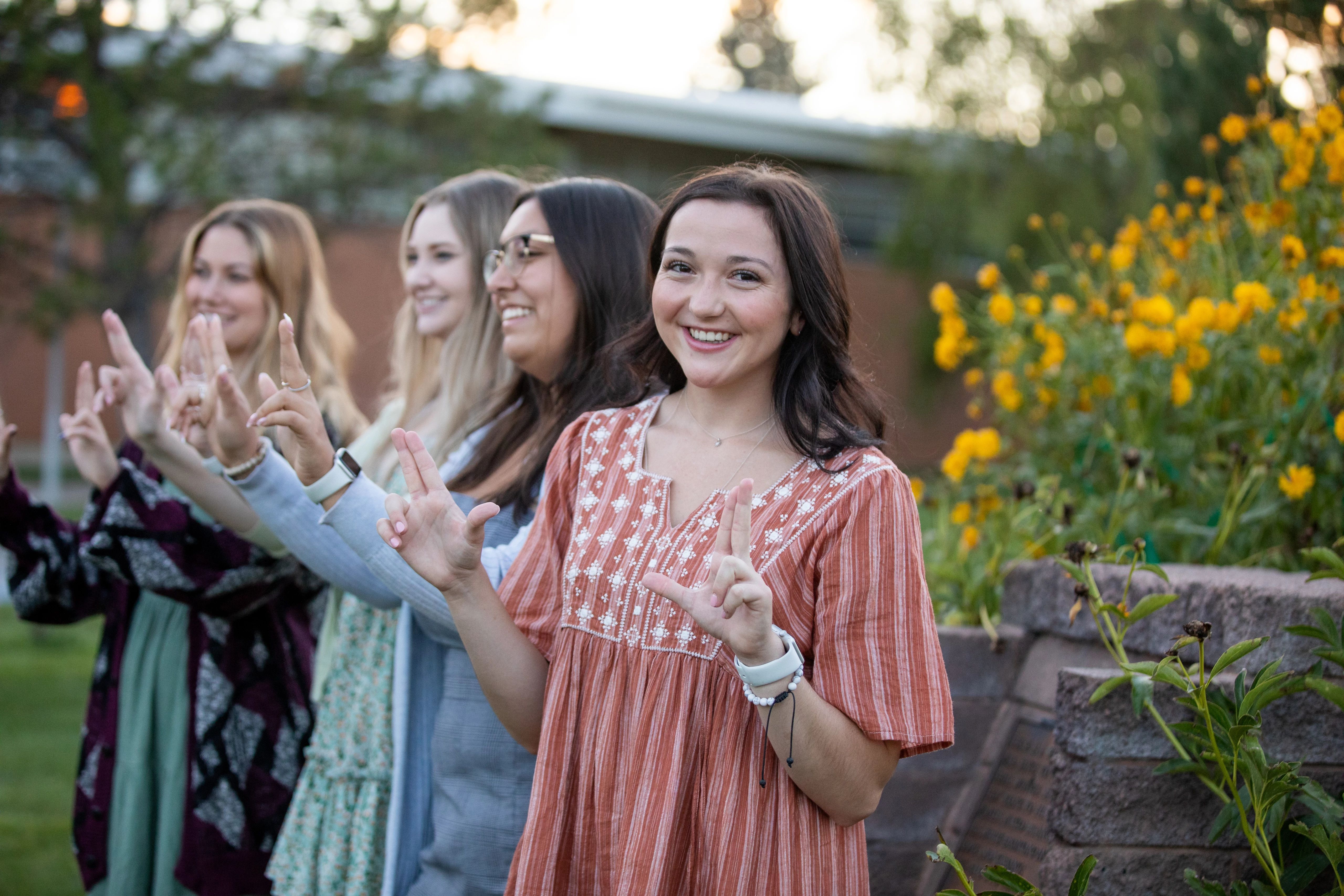 N A U students posing for camera outside, holding up both of their hands in the Lumberjack hand sign.