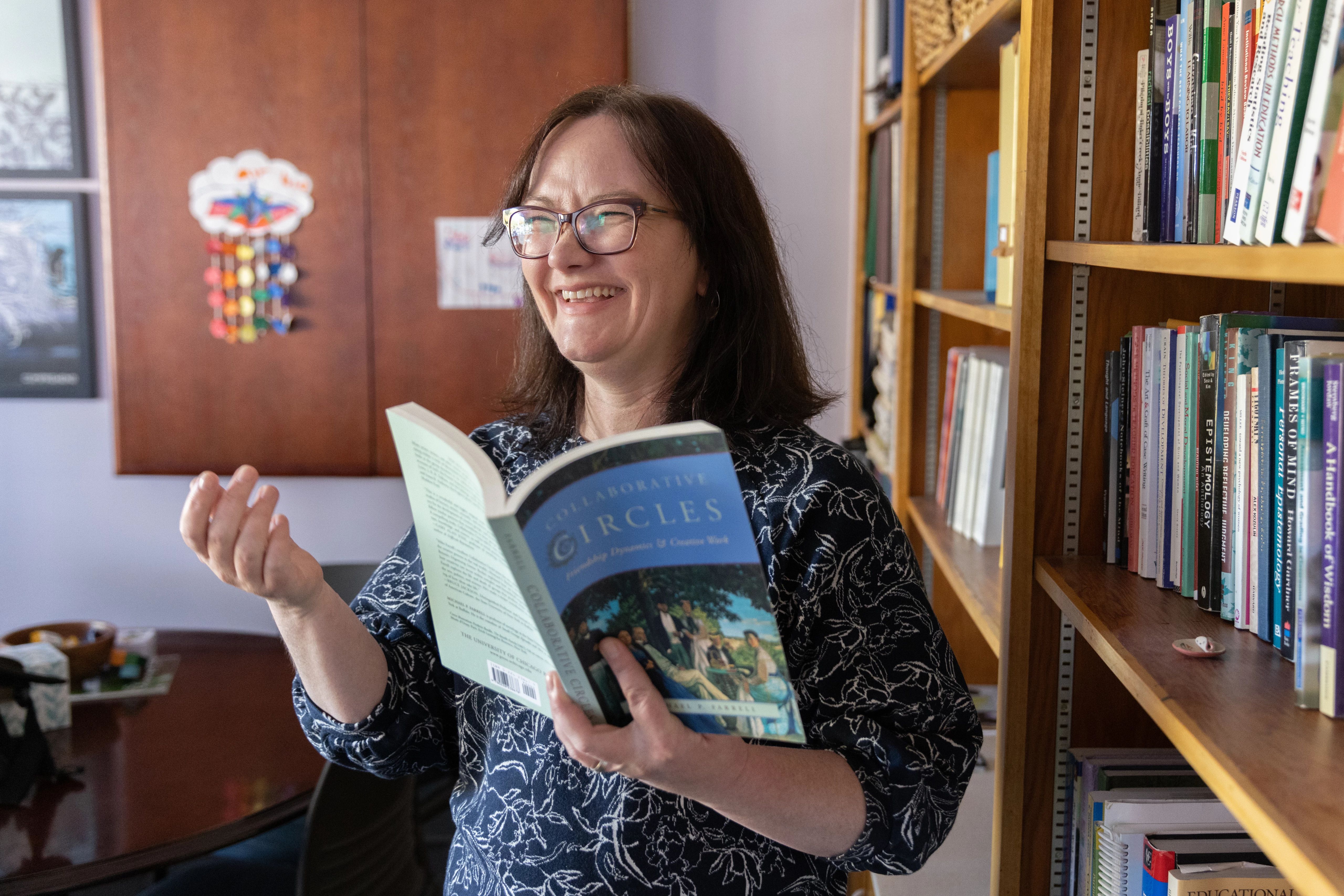 N A U faculty member reads book next to book shelf and smiles.