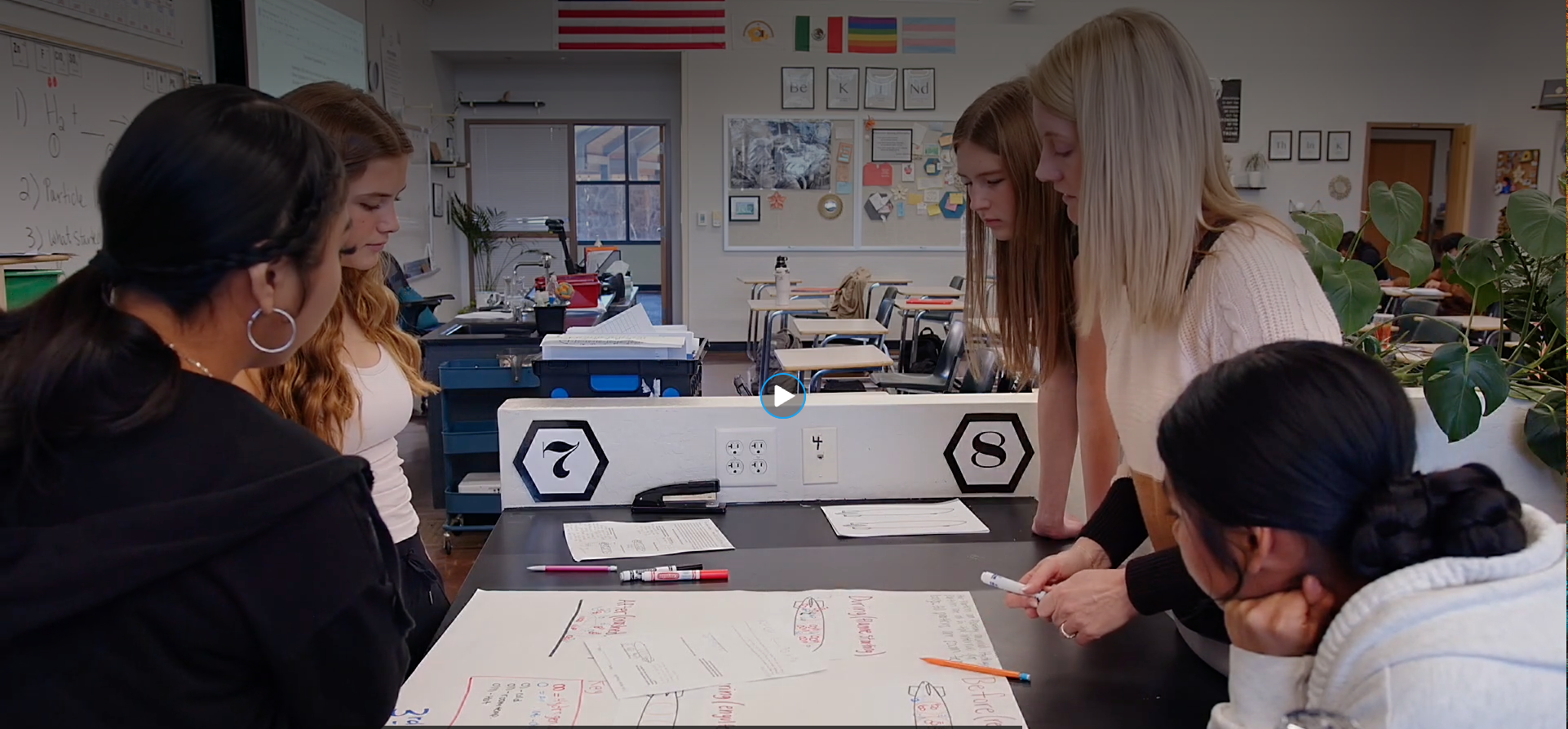 Science teacher Jennifer Askew works with a small group of students gathered around a classroom lab table as they examine and discuss written models.