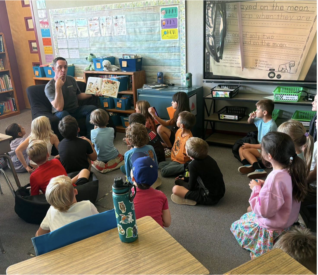Arizona Teacher Residency participant Michael Lamb sits at the front of a classroom holding an open picture book while a group of second-grade students sit around him listening and participating in the lesson.
