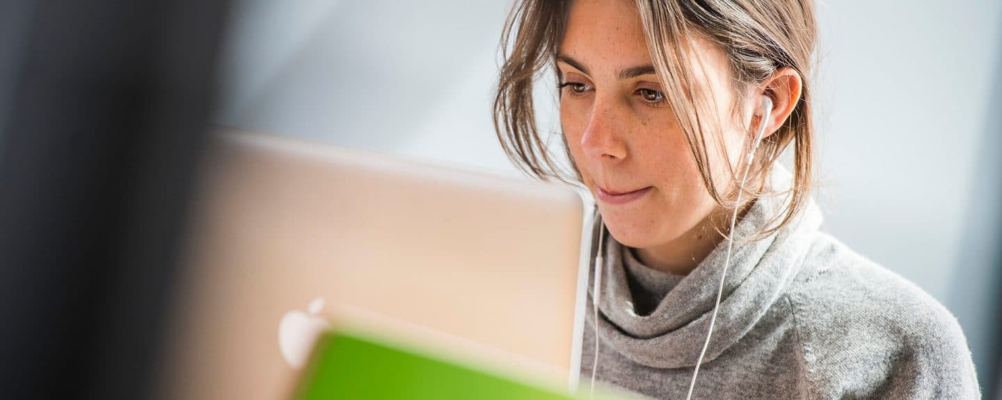 Student wearing earbuds while studying on MacBook laptop.