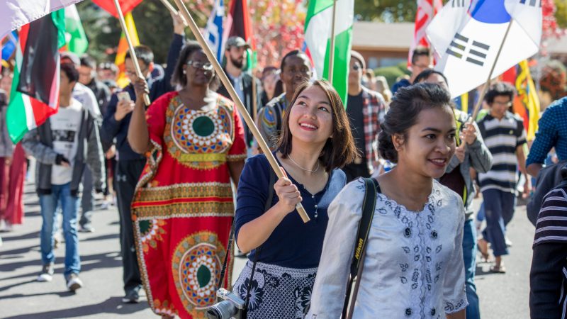 Students walk in a parade with international flags.