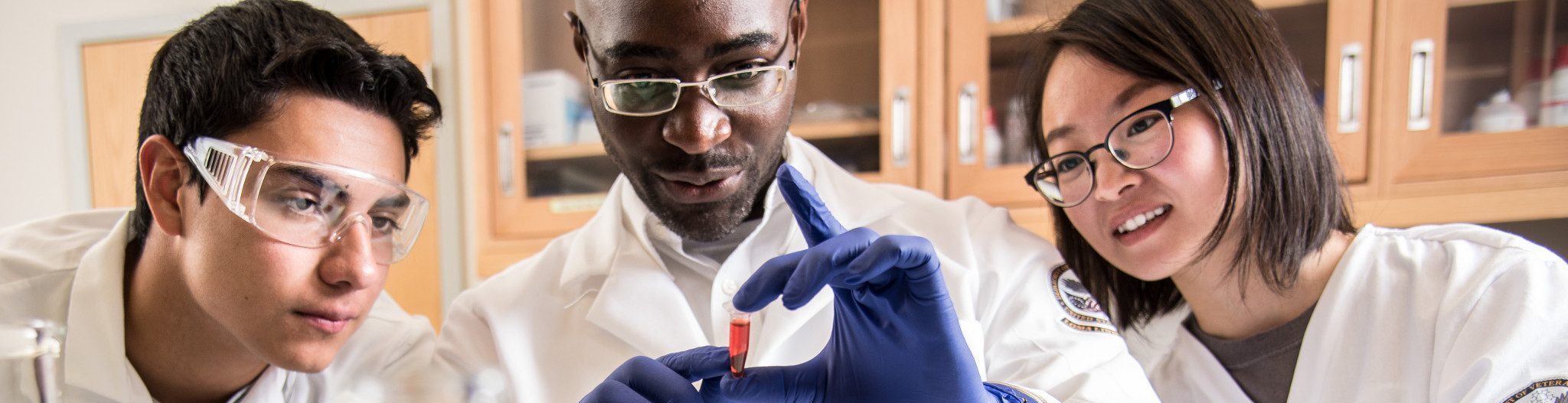 Students in lab coats examining a vial.