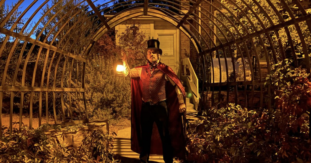 A man with a top hat and cape holding a lantern.