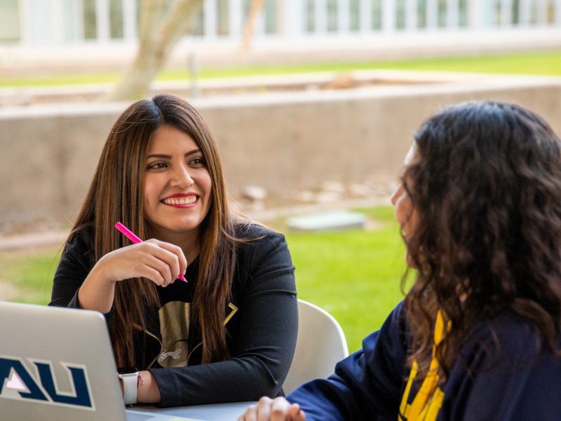 Two N A U–Yuma students working on laptop outside.