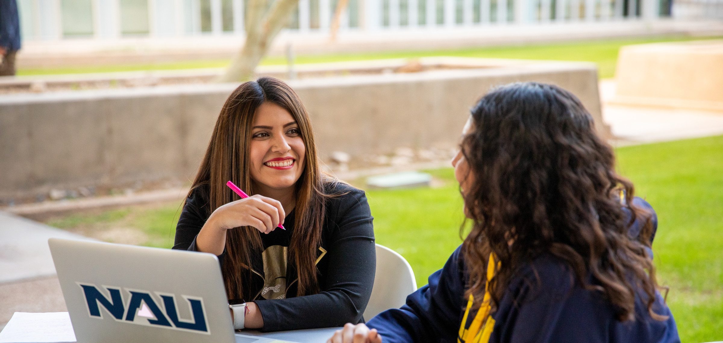 Two N A U–Yuma students working on laptop outside.