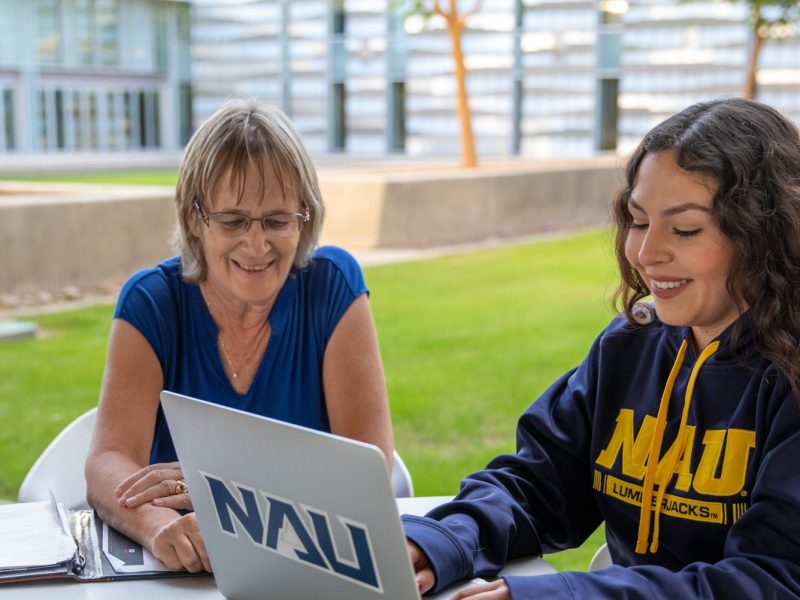 Student and faculty working on laptop outside.