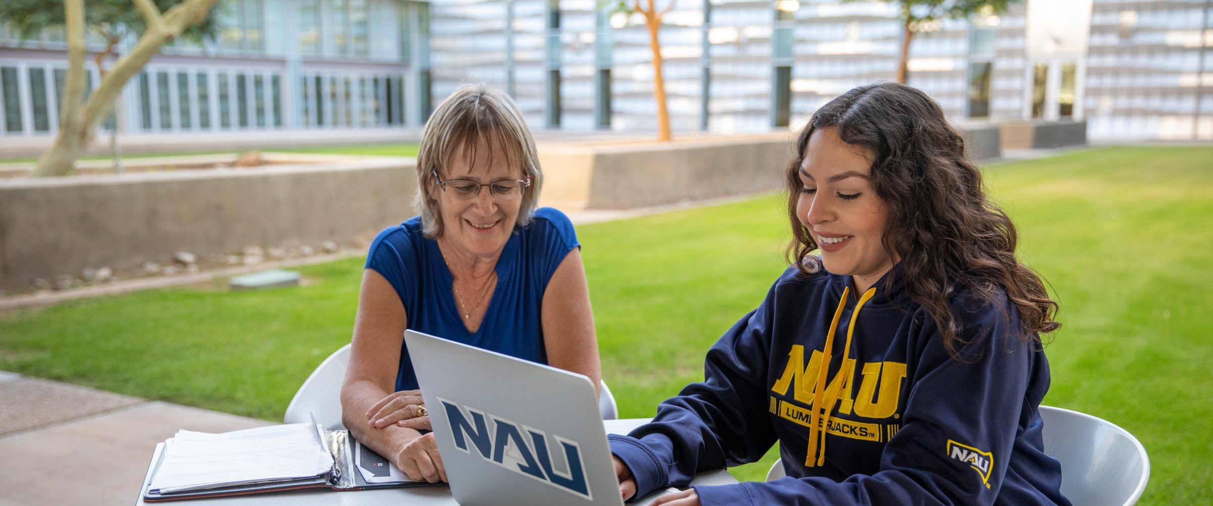 Student and faculty working on laptop outside.