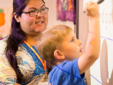 College of education student teacher helping a child write on a smart board.