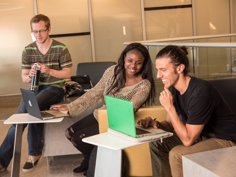 Three students study around a laptop.