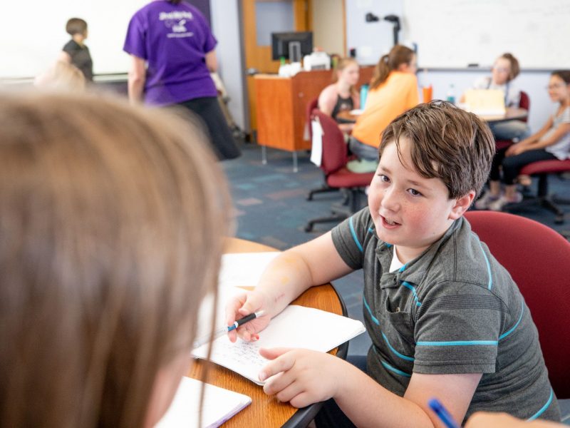 Young child talks with teacher as he works on an assignment.