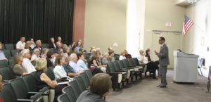 Frederick W. Gooding Jr. gestures while speaking in front of a seated crowd