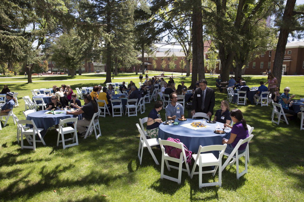 NAU alumni sitting at tables under trees on North Quad