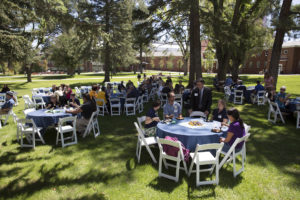 NAU alumni sitting at tables under trees on North Quad