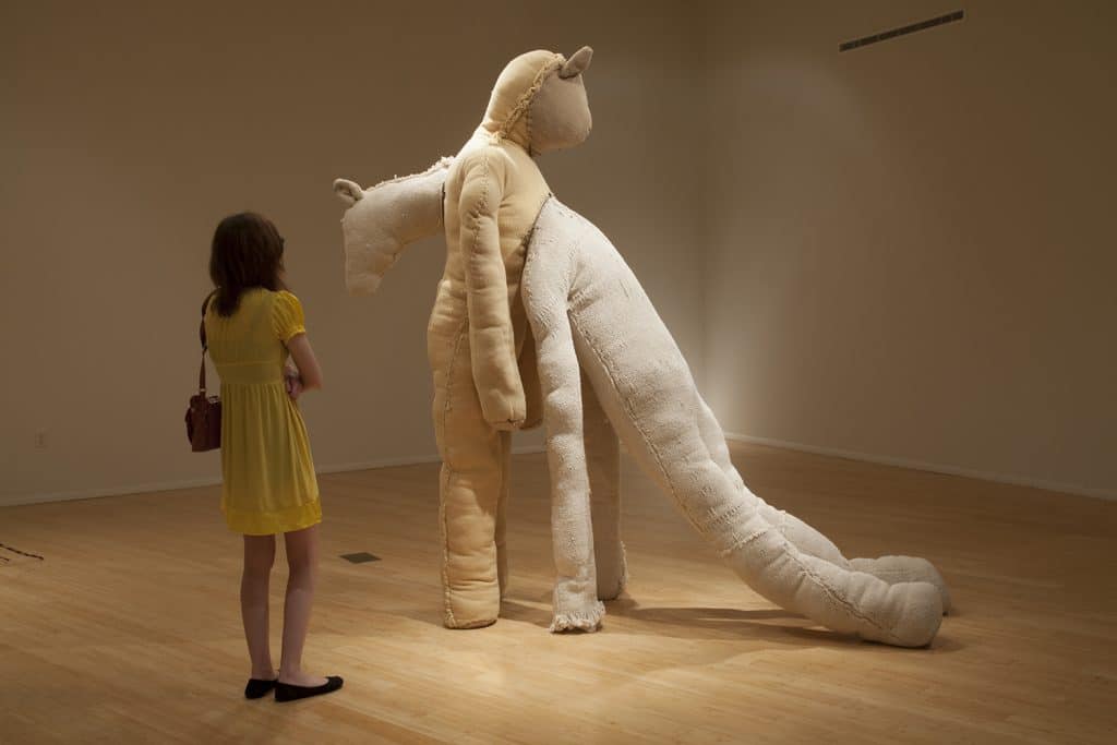 Spectator viewing a tall, humanoid sculpture where one person is leaning into another.