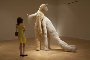 Spectator viewing a tall, humanoid sculpture where one person is leaning into another.