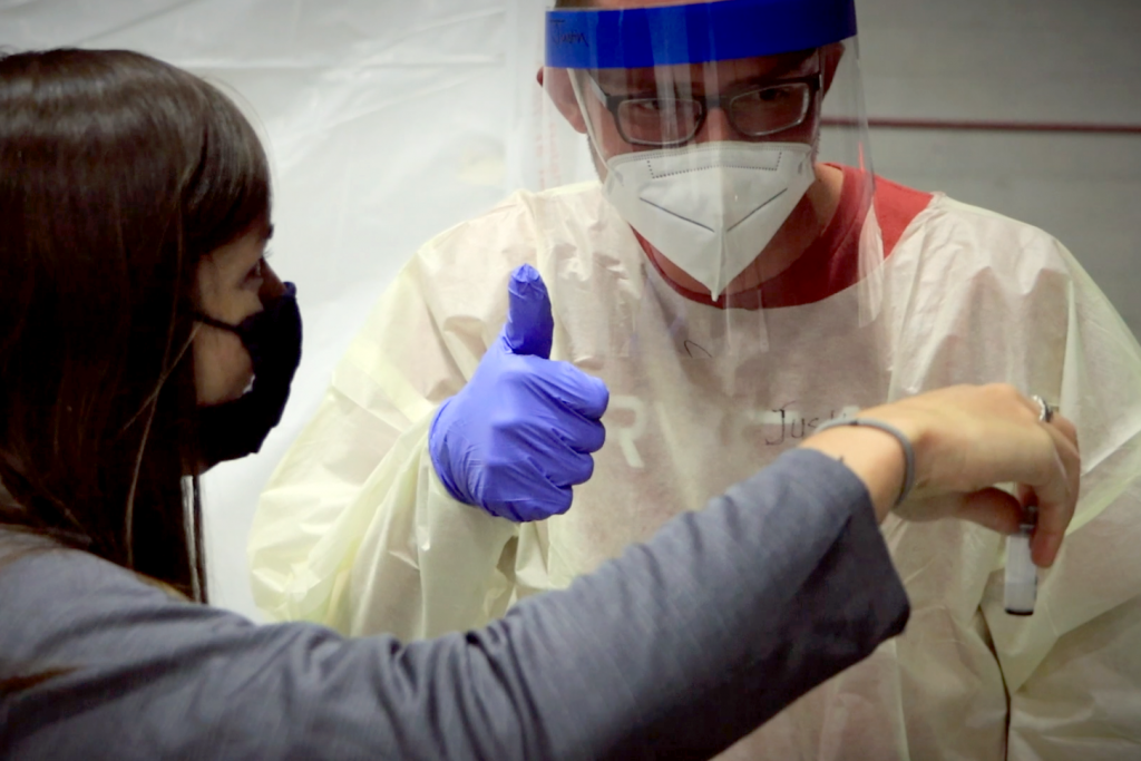 Guy in PPE gives woman a "thumbs up" for producing a good saliva sample