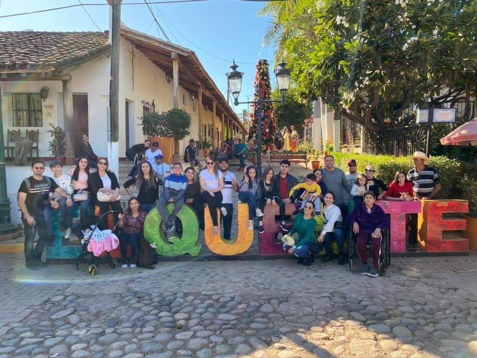 Large group photo in front of sign saying Quelite, the town where Acosta's family is from.
