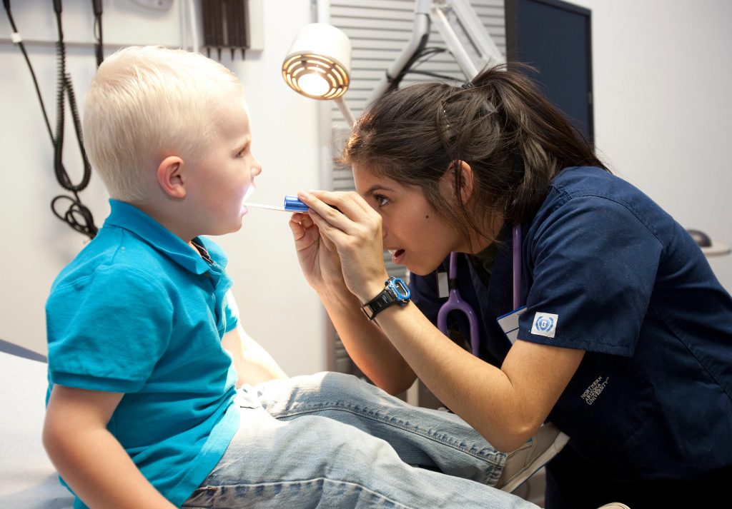 A nursing student uses a tongue depressor to check a young child's throat.
