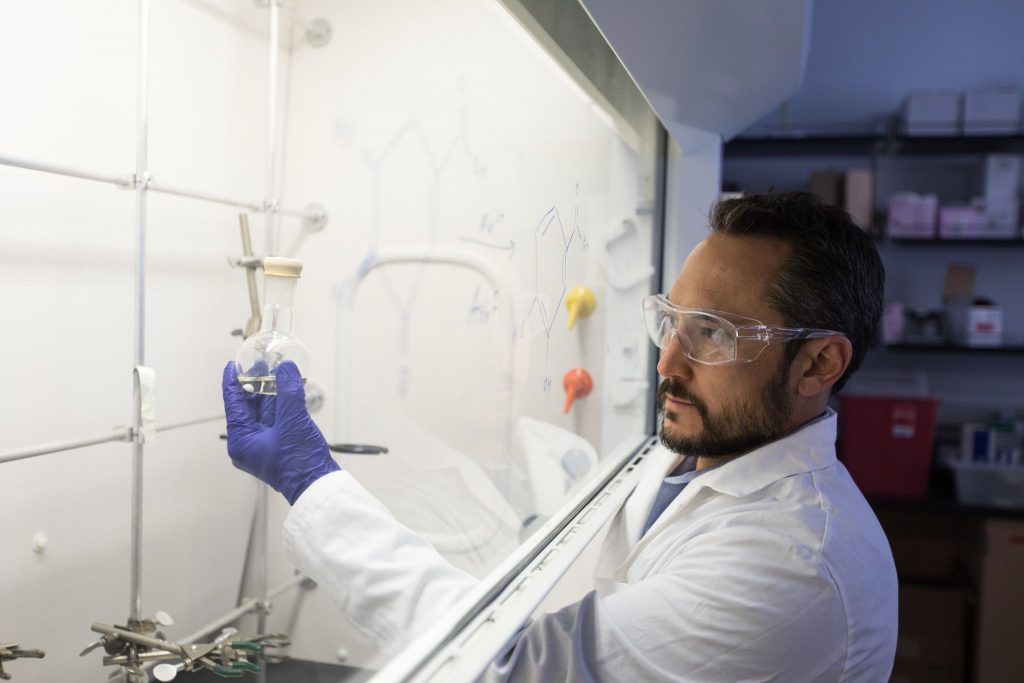 Rob Kellar holds a beaker behind a hood.