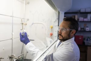 Rob Kellar holds a beaker behind a hood.