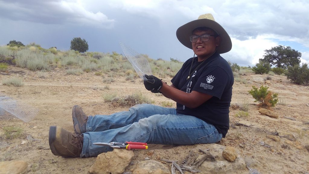 A student sits on the ground putting together planting equipment.